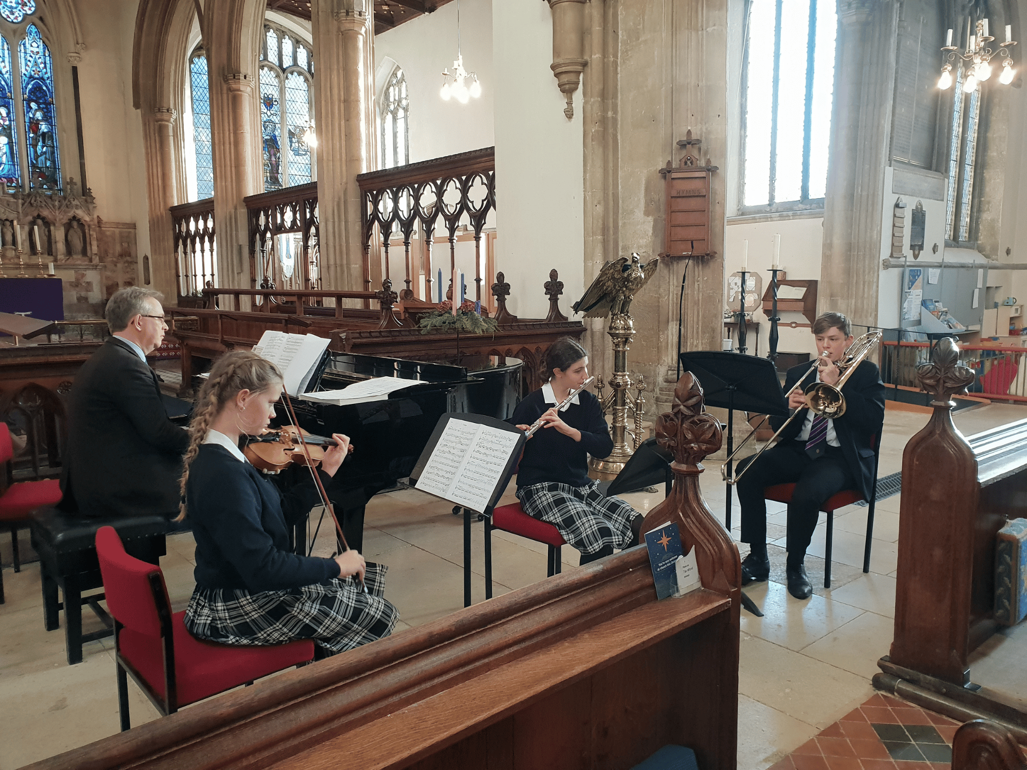 An ensemble of piano, violin, flute and trombone perform in concert in a church