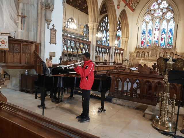 Student plays the trumpet, accompanied on the piano, in a recital in a church