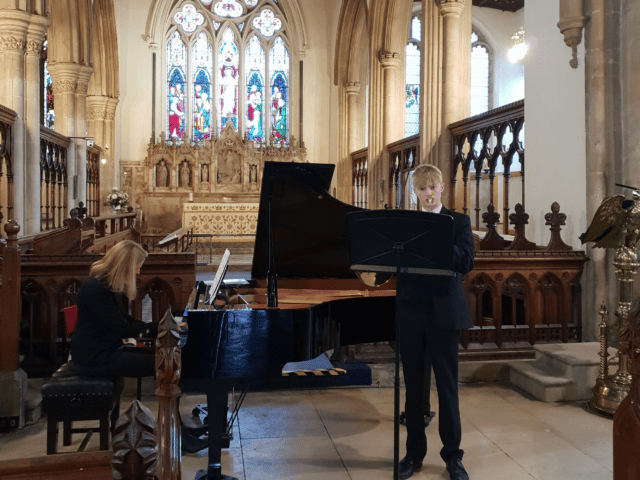 A student plays the French horn in a recital in a church