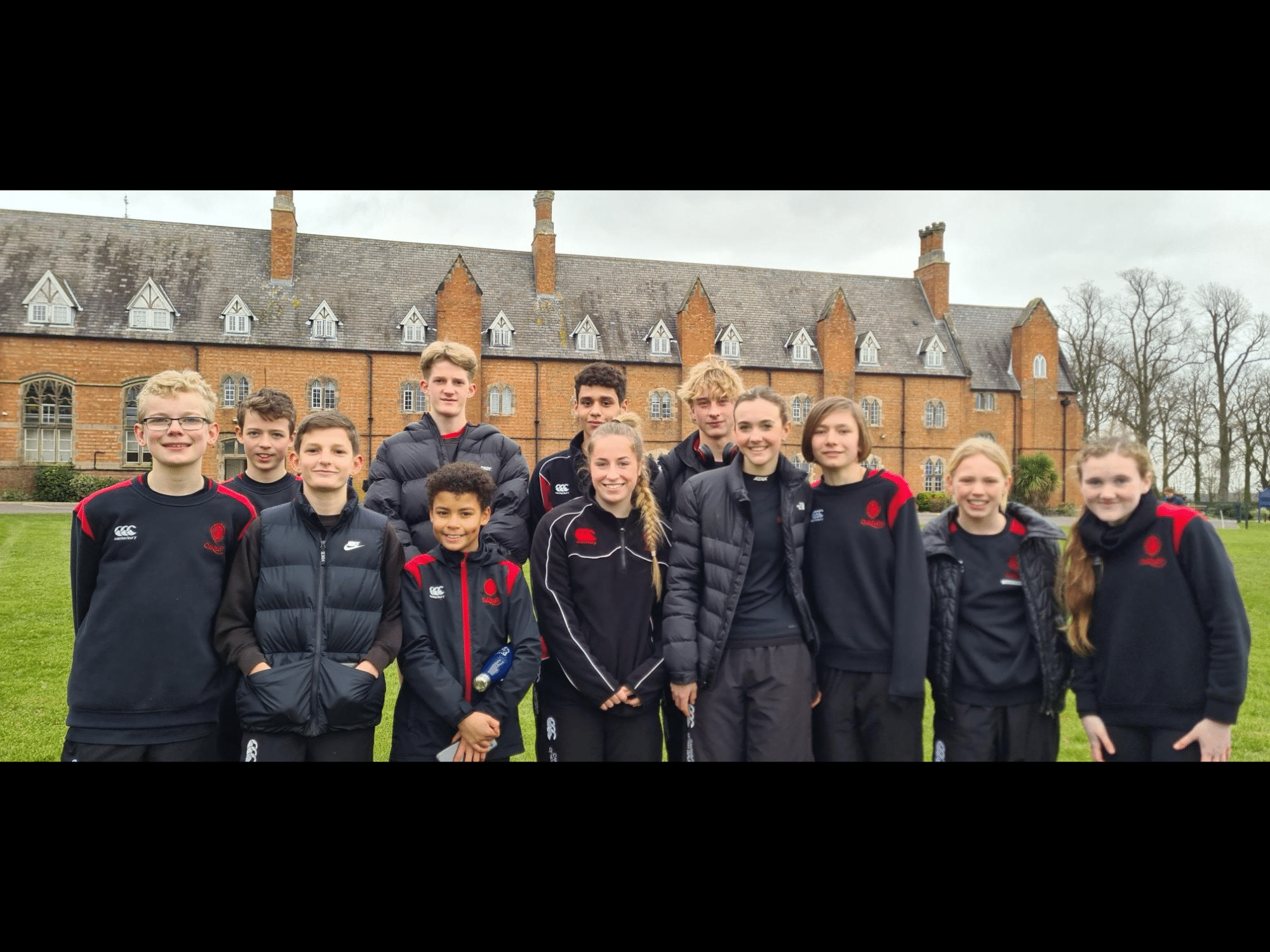 Pupils wearing black and red standing in front of School after running Cross Country