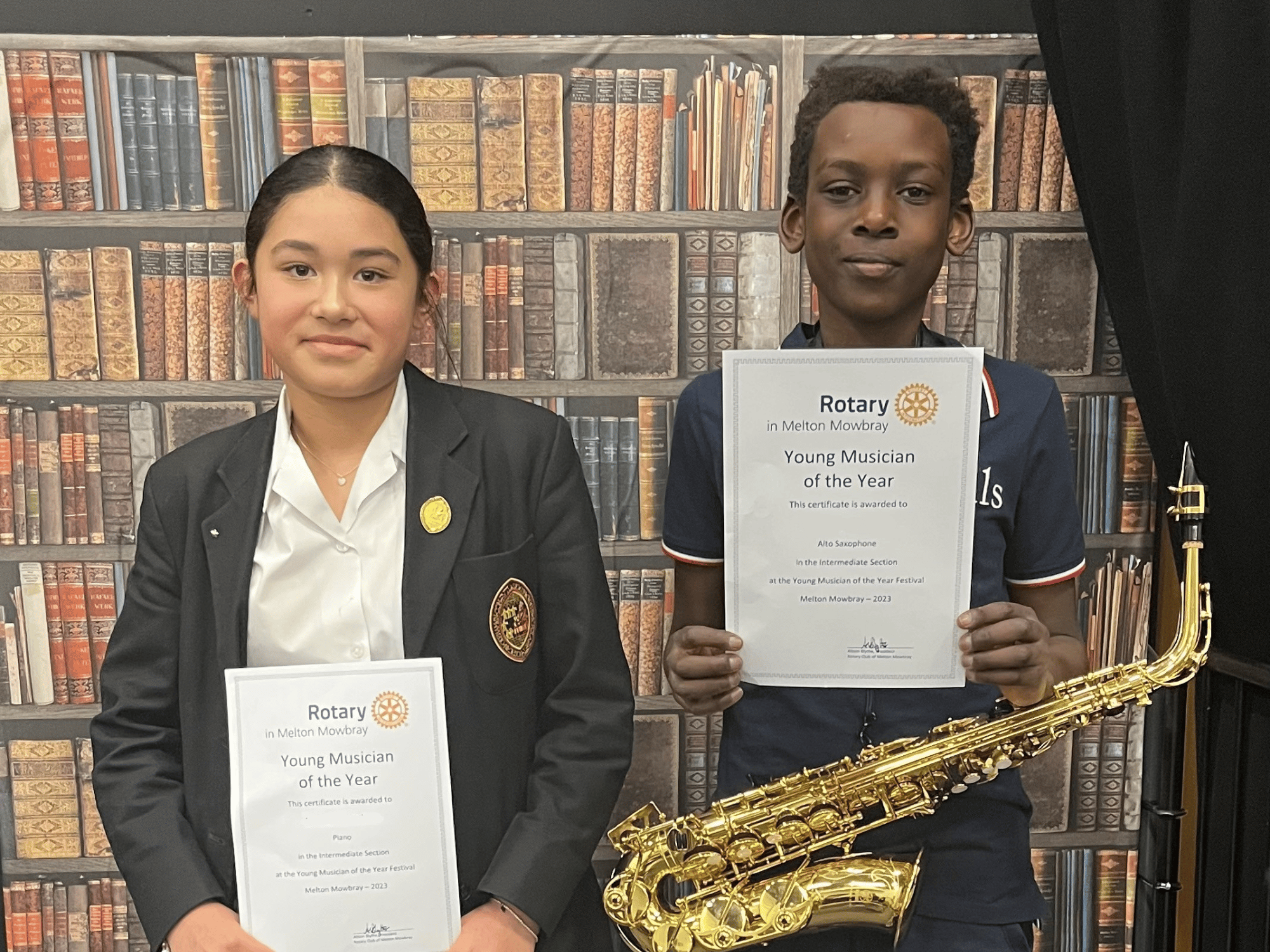 Two students smile with certificates, one with an alto saxophone