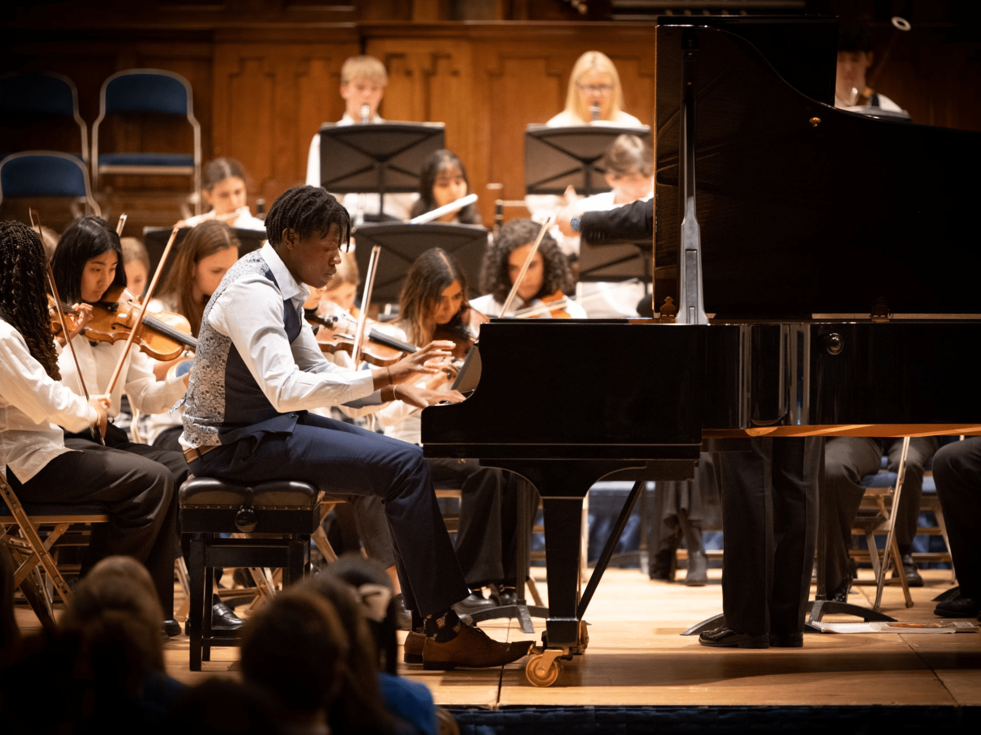 Close up shot of student playing piano with orchestra behind