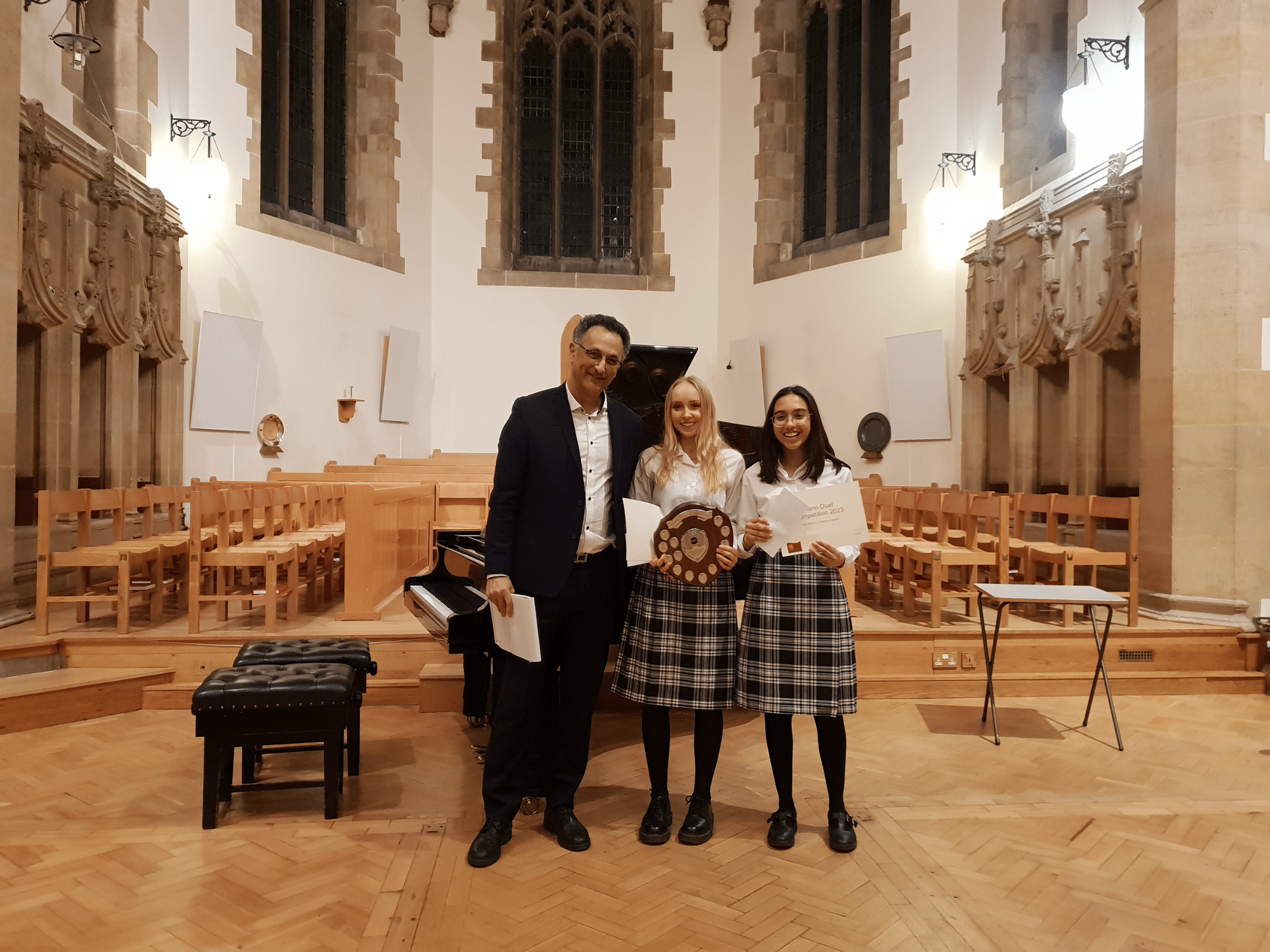 Two students smile with certificates and a shield after winning piano competition