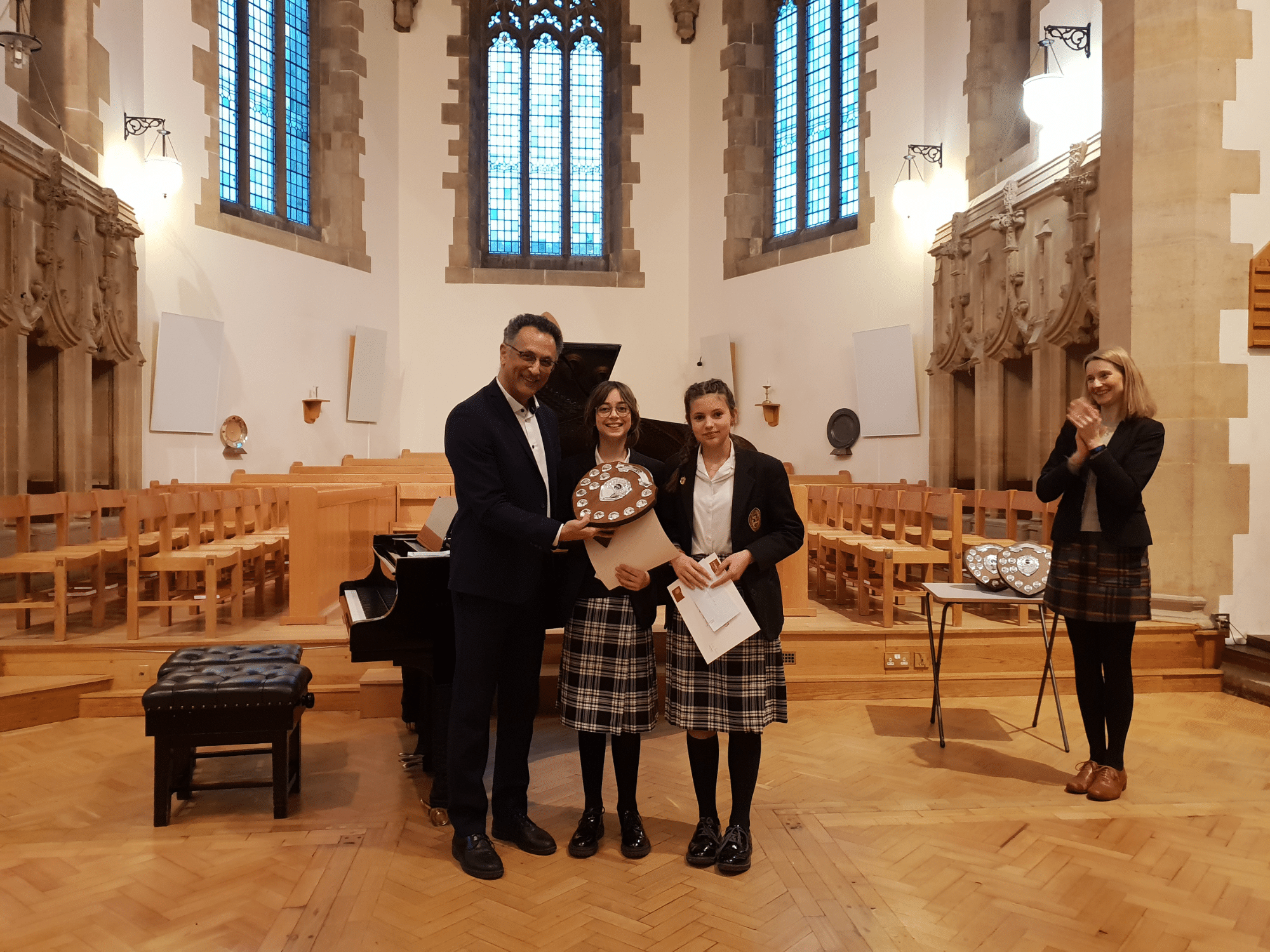 Two students smile with certificates and a shield after winning piano competition