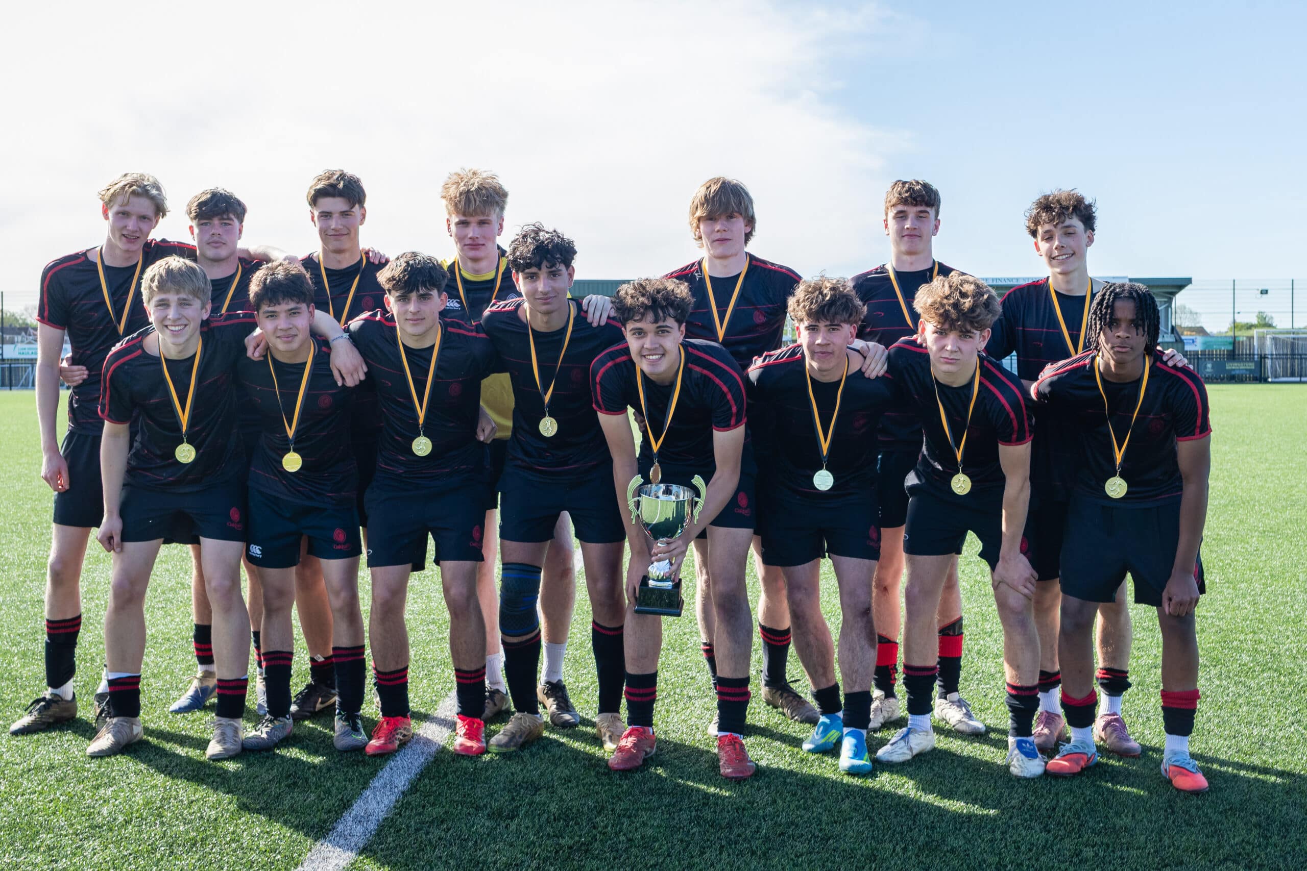A group of boys in football kit wearing medals round their neck and the centre figure holding a cup