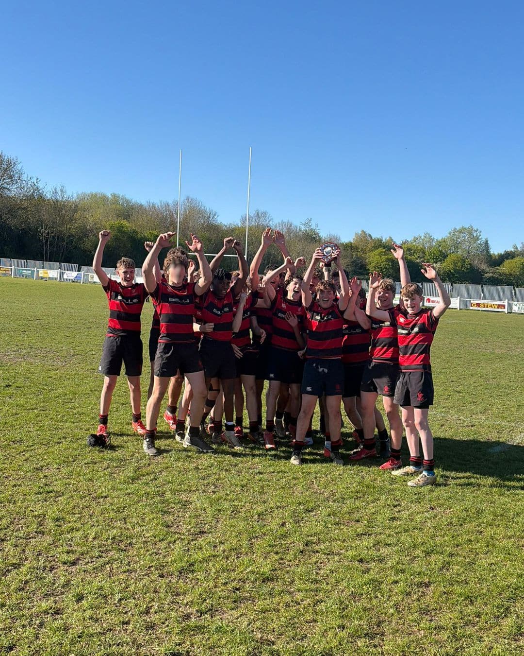 A group of boys in red and black striped rugby kit posing for a photo after winning a cup match
