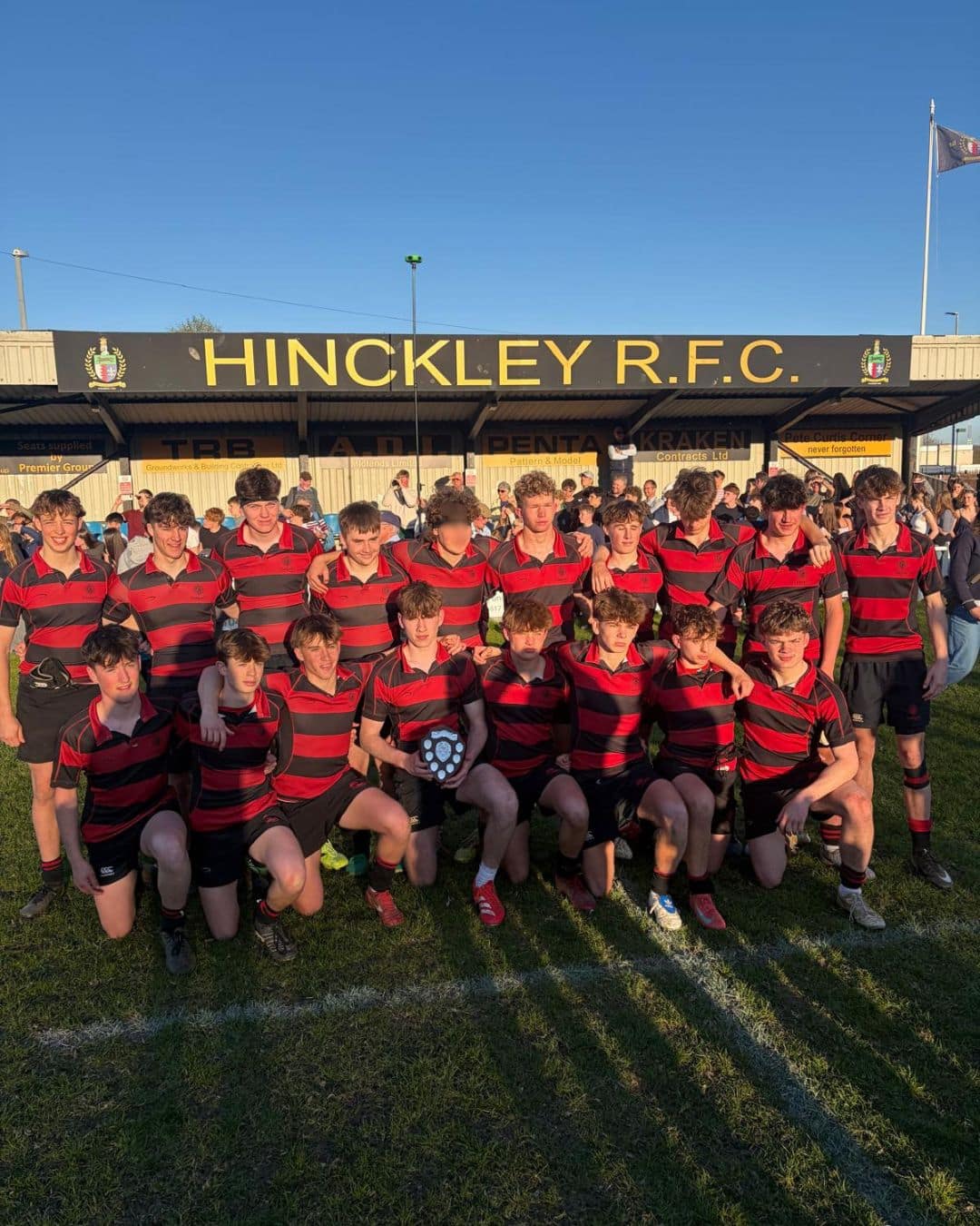 A group of boys in red and black striped rugby kit posing for a photo after winning a cup match