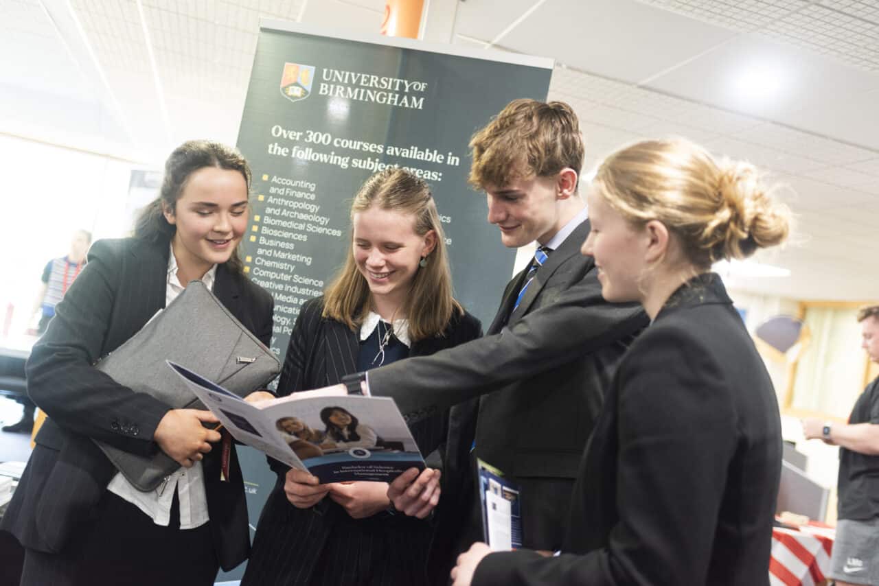 A group of four students looking at some university prospectuses with a University of Birmingham banner in the background.
